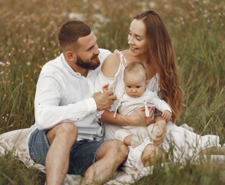 A joyful couple with their baby sitting on a blanket in a sunny meadow, embracing the beauty of summer.